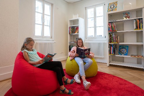 zwei Mädchen sitzen auf Sitzsäcken in der Stadtbücherei und schauen in ein Buch.