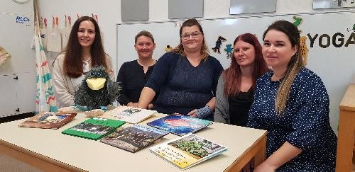 fünf Damen sitzen an einem Tisch auf dem sechs bunte Bücher für Kinder liegen