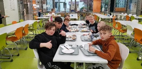 acht Jungs sitzen beim Frühstück an einem langen Tisch in der Mensa, links und rechts sind noch freie Tischreihen