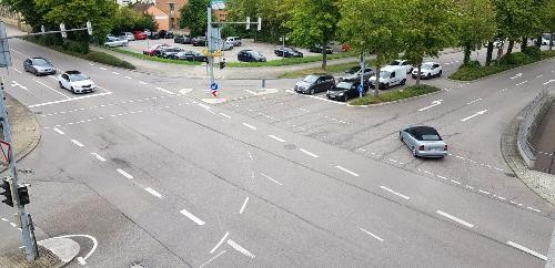 Blick auf die Straßenfläche der Kreuzung, 8 Autos warten an einer roten Ampel, ein Fahrzeugfährt üer die Kreuzung