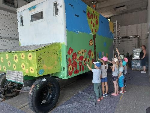 Eine Gruppe von Kindern steht vor einem bunt bemalten Bauwagen