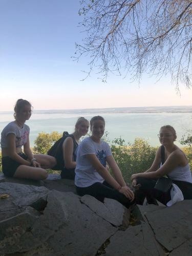 vier Mädchen sitzen auf großen Steinblöcken, im Hintergrund die Wasserfläche eines Sees