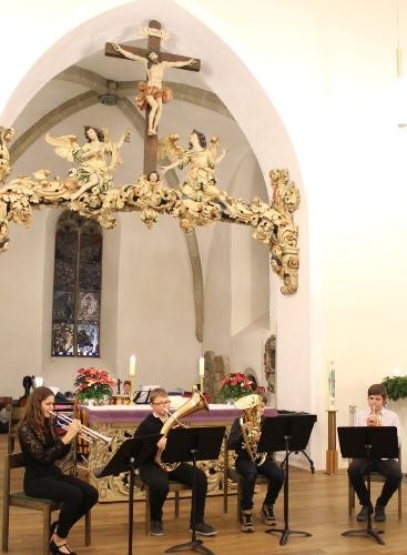 vier Blechbläser sitzen untern einem Triumphkreuz in der Kirche, vor ihnen Notenständer