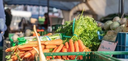 frisches Gemüse an einem Marktstand, im Vordergrund orangefarbene Karotten