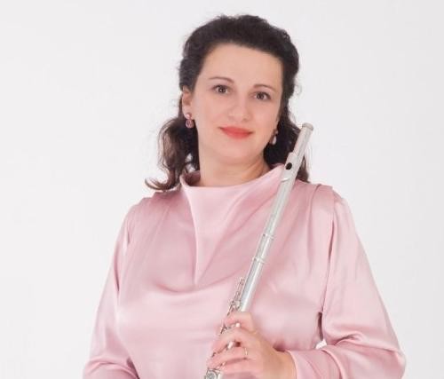 Dame in rosa Bluse hält eine Querflöte vor sich in Händen