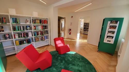 Blick in einen Raum der Bücherei, zwei rote Sessel und weiße Regale gefüllt mit Büchern