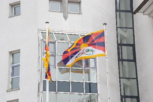 Blick auf zwei Tibetfahnen, die außen an der weißen Rathausfassade wehen