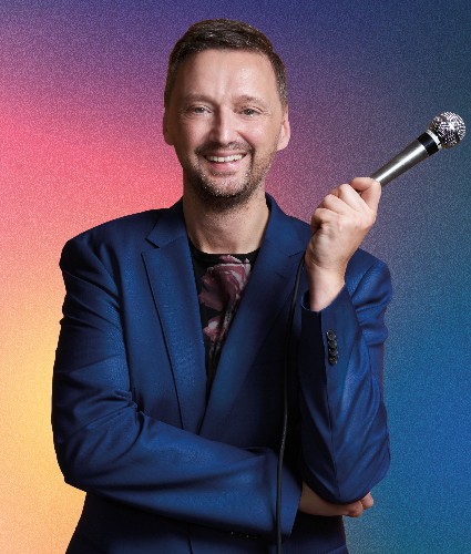 lächelnder Mann mit blauem Blazer und Mikro in der Hand