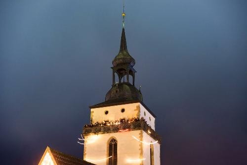 Blick auf den Kirchturm, Laternen werden vom Balkon geschwenkt und zeichnen Lichtbögen, die an Engel erinnenr