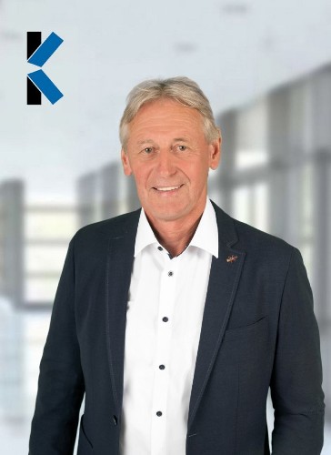 Brustbild eines Herren, der ein schwarzes Sakko über einem weißen Hemd  trägt