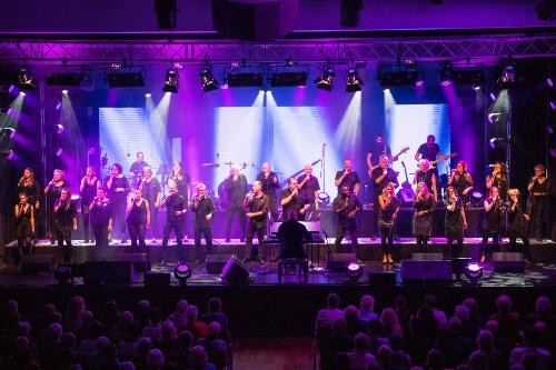 Großer gemischter Chor in Aktion auf einer großen Bühne die im Grund lila bleuchtet ist