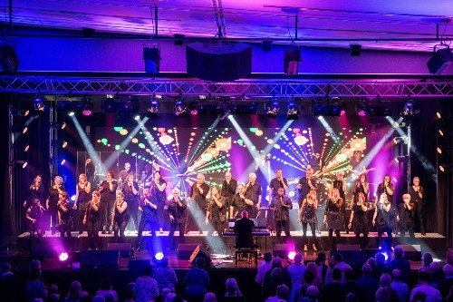 Großer gemischer Chor in Aktion auf einer großen Bühne die im Grund lila beleuchtet ist