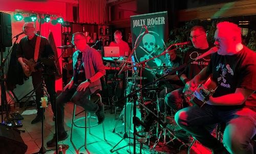 fünf Musiker an Gitarren und Schlagzeug in rot-grünes Dämmerlicht getaucht auf der Bühne in Aktion