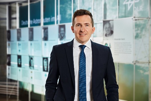 Porträtfoto von Bürgermeister Neumann. Er trägt ein schwarzes Sakko, weißes Hemd, blaue Krawatte