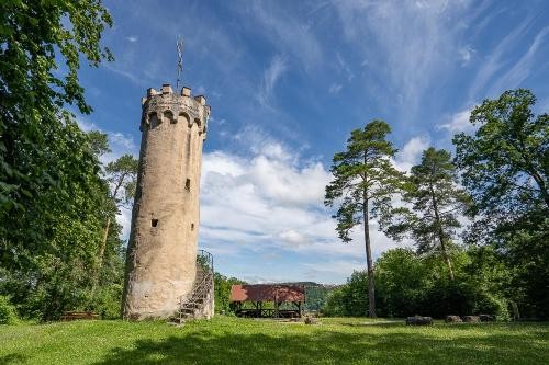 links im Bild ein hoher historischer Turm mit Außentreppe, im Hintergrund eine Schutzhütte aus Holz und ein wenig Blick ins Tal