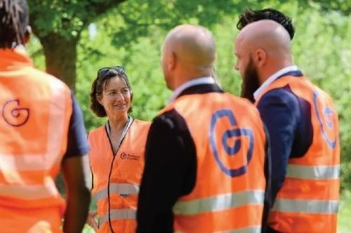Personen mit einer orangenen Warnweste stehen im grünen.