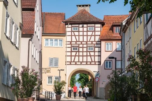 Stadttor mit Häusern und Personen die durch die Stadt schlendern.