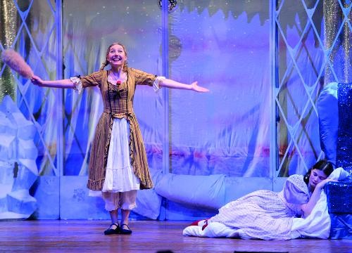 Eine Frau steht auf eine rBühne in kaltem Licht. rechts im Bild liegt eine FRau schlafend auf dem Boden.