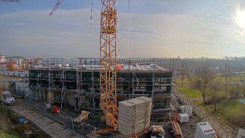 Blick auf die Baustelle: im Vordergrund ein gelber Kran, dahinter ein eingerüsteter Rohbau mit 2 Stockwerken