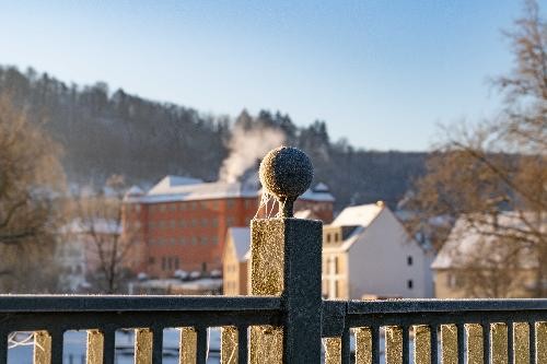 Blick über das Brückengeländer der Kocherbrücke zum Schloss Bartenau. Das DAch ist mit Schnee bedeckt.