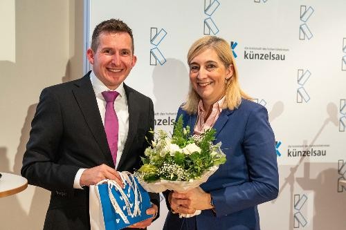 Bürgermeister Stefan Neumann in Anzug und Krawatte mit kleinem Present in der Hand. Neben ihm steht Nina Warken mit einem Blumenstraß.