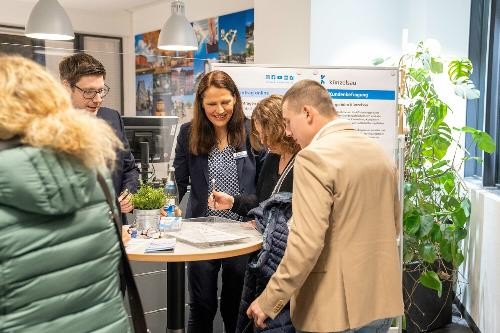zwei Damen und zwei Herren stehen um einen Stehtisch und blicken auf Informationsmaterial dort