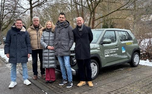 fünf Personen stehen vor einem gespendeten Auto in grüner Farbe.