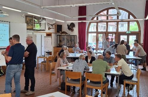 In einem großen Raum sitzen und stehen viele Menschen und reden und diskutieren.