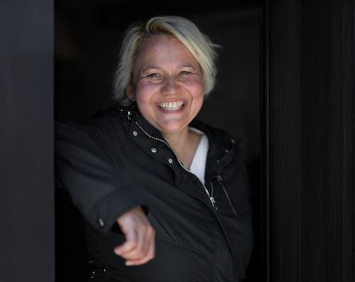 Ein Portait von einer Frau. Sie lächelt und hat ein schwarzes Oberteil an und kürzere blonde Haare.