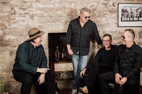 Vier Männer, davon drei sitzend und einer stehend, schauen sich freudig vor einer Steinwand an.