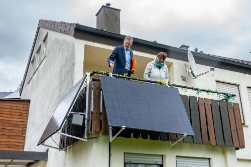 Auf einem Balkon von einem Haus stehen zwei Personen und schauen sich die Photovoltaik-Anlage an.