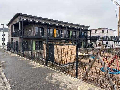 Ein kindgerecht gestaltetes Gebäude der Krippe in Künzelsau, davor ein Spielplatz mit Spielgeräten und Sandbereich. Das Gelände wirkt einladend und sicher für Kleinkinder im Alter von ein bis zwei Jahren.