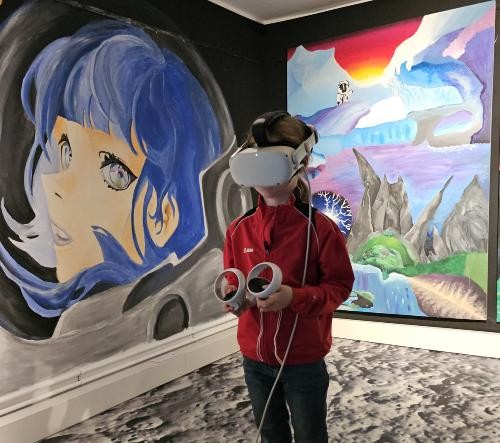 Ein kleines Mädchen steht in der Space Art Ausstellung mit vielen bunten Bilder im Raum. Sie hat eine VR-Brille auf dem Kopg