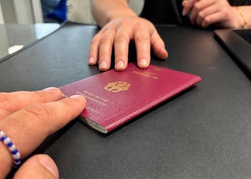 Nahaufnahme einer Person, die einen Reisepass über die Theke eines Bürgerbüros an eine Mitarbeiterin übergibt. Im Fokus stehen die Hände und das Reisedokument.