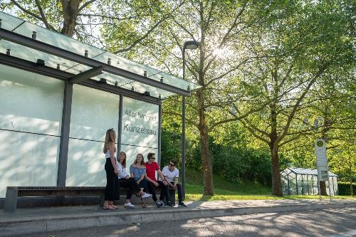 Mehrere Menschen stehen und gehen vor dem Alten Bahnhof in Künzelsau. Das Bild zeigt den öffentlichen Platz im Alltag.