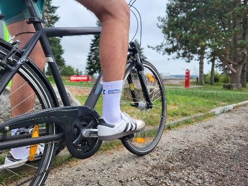 Nahaufnahme einer Person auf einem Fahrrad im Freien. Zu sehen sind Fahrrad, Beine und Schuhe der radelnden Person. Im Hintergrund befinden sich Bäume und eine Grünfläche. Das Bild veranschaulicht die Teilnahme am STADTRADELN in Künzelsau.