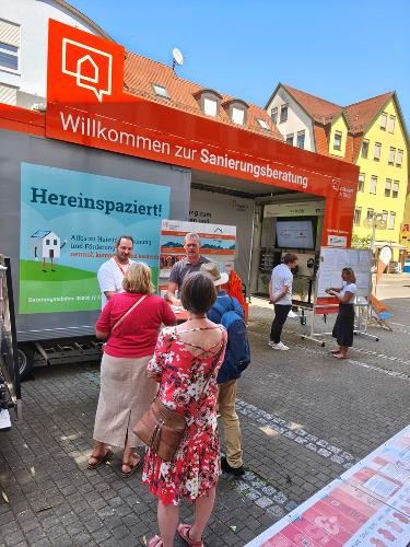 Mehrere Besucherinnen und Besucher führen vor dem Sanierungsmobil Beratungsgespräche zu den Themen Energieeffizienz und Gebäudesanierung.