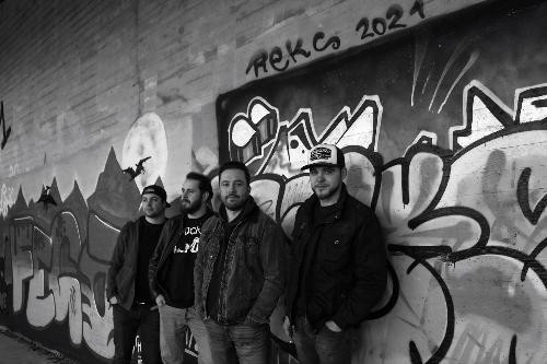Schwarz-Weiß-Foto der vierköpfigen Band WildVivid. Die Musiker stehen lässig nebeneinander vor einer großen Graffiti-Wand in einer Unterführung oder an einer Betonwand. Einige tragen Jacken und eine Person eine Baseballkappe. Im Hintergrund sind großflächige Graffiti, ein gemalter Mond und Bergmotive zu sehen. Die Band blickt in die Kamera und vermittelt einen modernen, rockigen Eindruck.