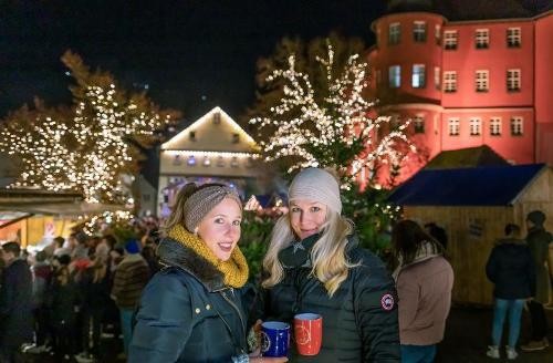 Advent am Schloss. Foto: Rolf Hartbrich Zwei Frauen die Glühwein trinken im Hintergrund der Weihnachtsmarkt am Schlossplatz.