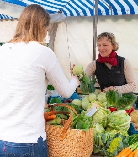 Frau kauft auf dem Wochenmarkt Gemüse ein.