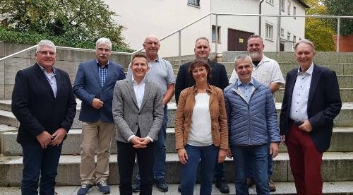 acht Herren und eine Damen stehen zum Gruppenfoto nebeneinander