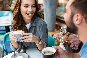 Eine Frau und ein Mann sitzen an einem runden Tisch und halten je eine Tasse Kaffee in der Hand