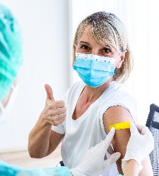 Frau die gerade geimpft wurde mit Maske und Daumen nach oben.