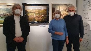 Drei Personen in der Ausstellung mit einem Landschaftsgemälde im Hintergrund