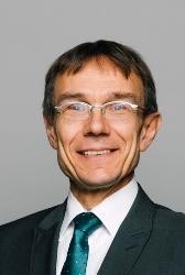 Porträtfoto: Herr mit Brille, Anzug und grüner Krawatte