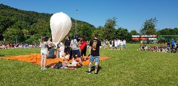 weißer Ballon wird mit Helium gefüllt, Schüler arbeiten mit, und viele Schüler schauen mi zu
