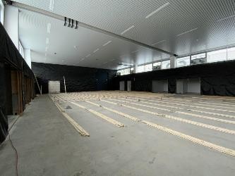 Blick in eine große Sporthalle: Die Wände sind schwarz verkleidet, auf dem Boden sind Holzdielen ausgelegt.