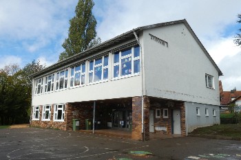 zweistöckiges Schulgebäude von außen, Eingangsbereich unten rechts, im  zweiten Stock durchgängige Fensterfront
