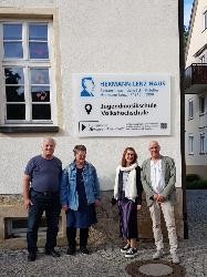 Vier Personen stehen vor dem neuen Schild am Hermann-Lenz-Haus.