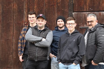 fünf Musiker stehen vor einem Holztor